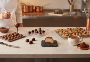 Bancada de cozinha profissional com barras, gotas, recheio e chocolate em pó organizados por aplicação.